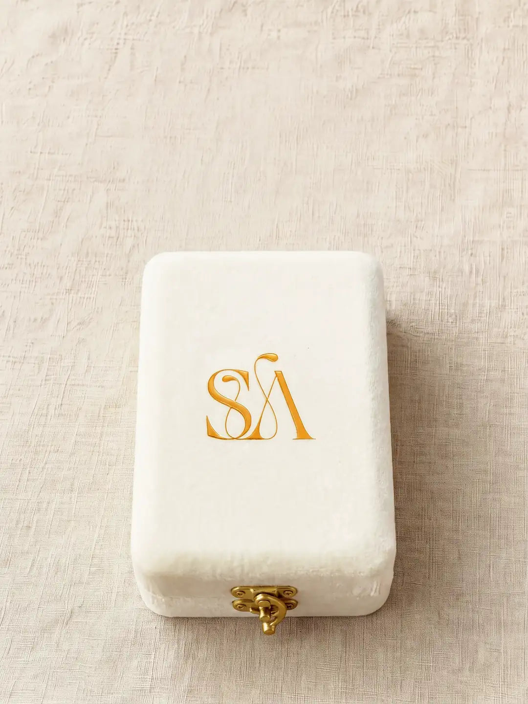 The cream velvet case, closed, a gold SA monogram on its lid and a small gold hook-and-eye clasp at the front