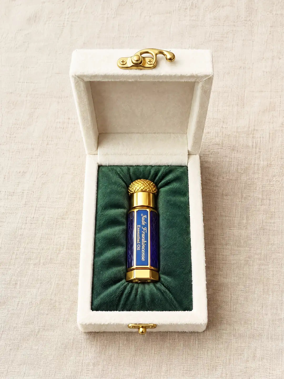 The case open: its lid lined in cream velvet, and the cobalt-blue bottle with its gold cap lying in deep green velvet. The label reads Jade Frankincense Essential Oil.