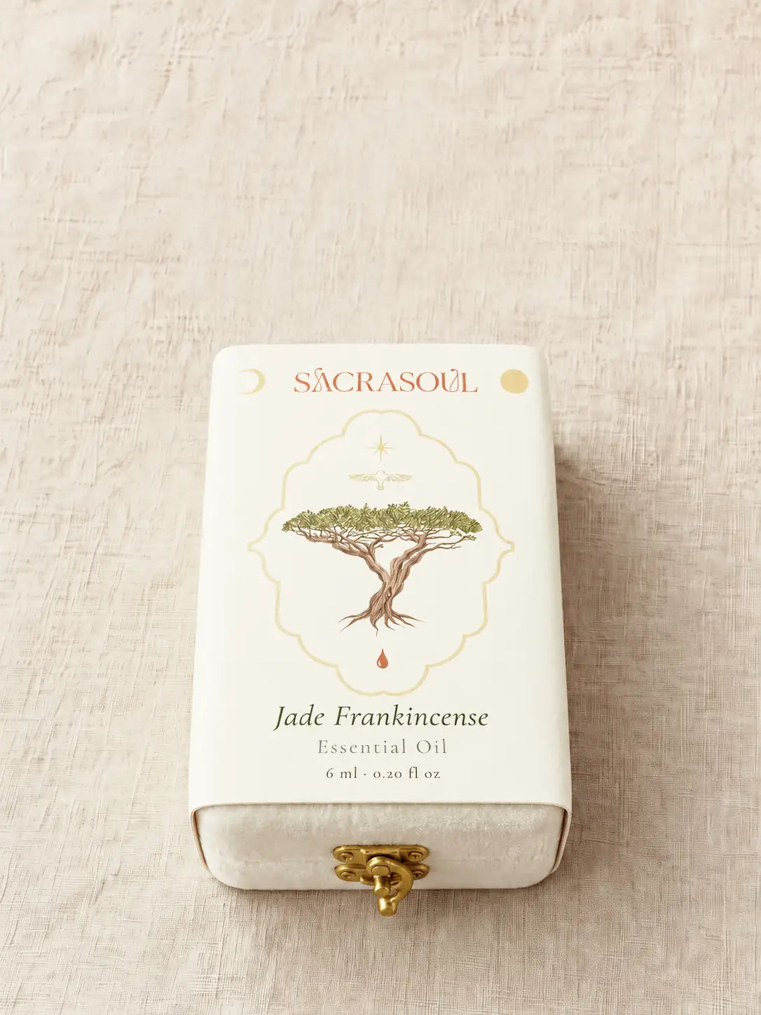 The case in its printed white sleeve on linen. The sleeve reads SACRASOUL, then a frankincense tree in a gold cartouche, then Jade Frankincense, Essential Oil, 6 ml · 0.20 fl oz. The gold clasp shows at its open end.